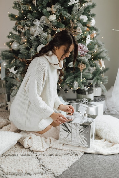 Beautiful girl looks very happy and unpacks a gift on a Christmas tree background