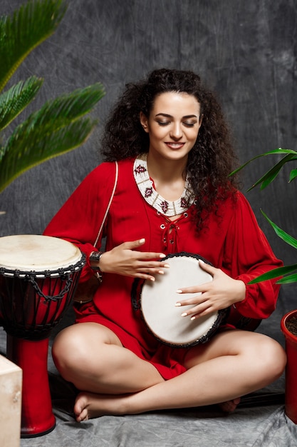 Free Photo beautiful girl playing drum in tropical plants over grey wall