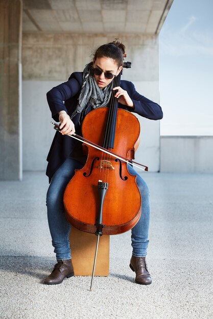 beautiful girl plays the cello with passion in a concrete environment