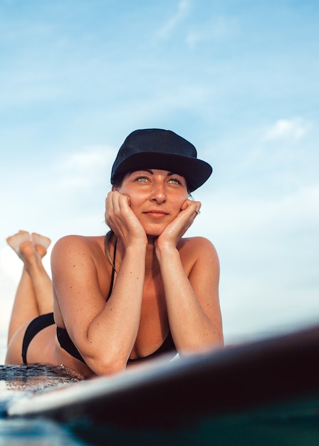 Beautiful girl posing sitting on a surfboard in the ocean