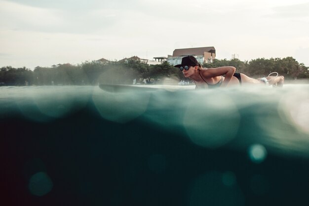 Beautiful girl posing sitting on a surfboard in the ocean