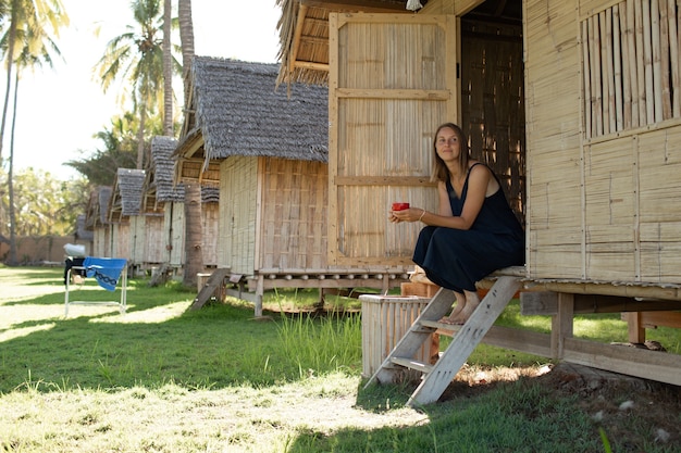 Free photo beautiful girl sits near the bungalow and drinks coffee.