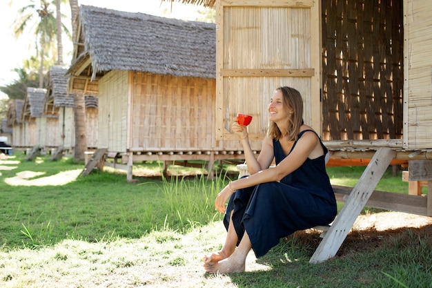 Free photo beautiful girl sits near the bungalow and drinks coffee.