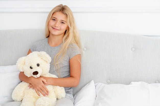 Beautiful girl sitting in bed with her teddy bear