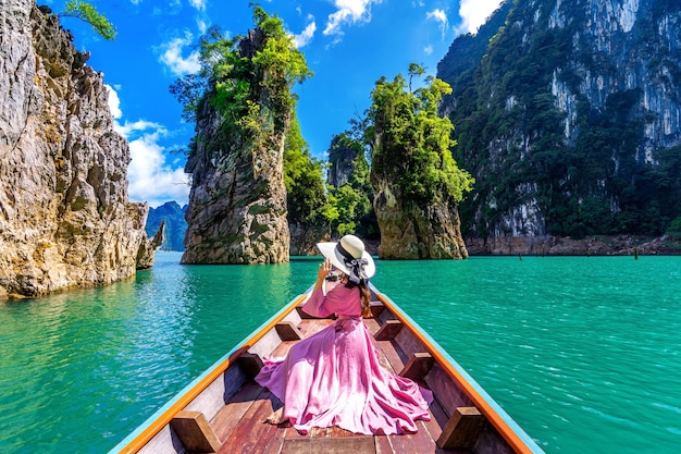 Free photo beautiful girl sitting on the boat and looking to mountains in ratchaprapha dam at khao sok national park, surat thani province, thailand.