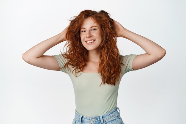 Free photo beautiful girl smiles and looks happy resting with hands behind head lay back and watch something standing over white background copy space