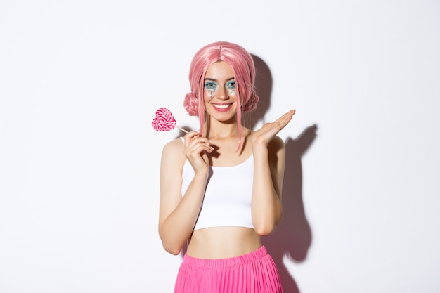 Free photo beautiful girl smiling, wearing pink wig and fairy costume, holding heart-shaped candy, standing.