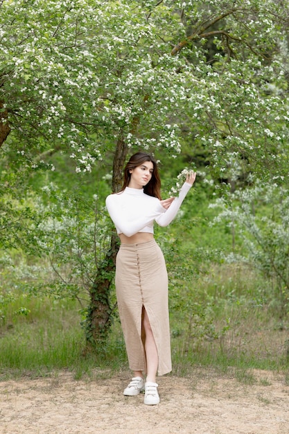 Free photo beautiful girl standing in blooming park holding tree branch looking forward admiring