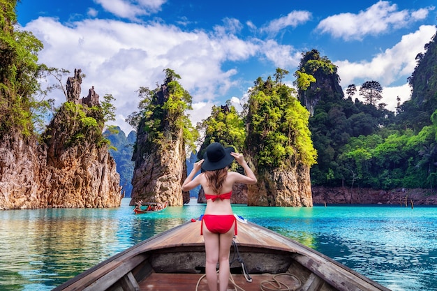 Beautiful girl standing on the boat and looking to mountains in Ratchaprapha Dam at Khao Sok National Park, Surat Thani Province, Thailand.