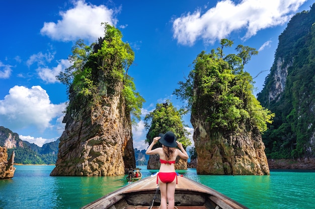 Free photo beautiful girl standing on the boat and looking to mountains in ratchaprapha dam at khao sok national park, surat thani province, thailand.