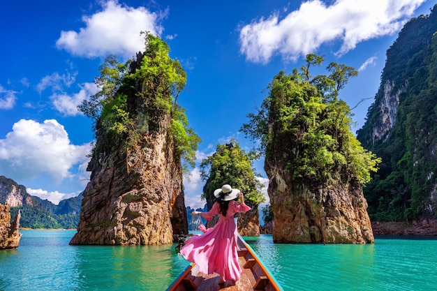 Beautiful girl standing on the boat and looking to mountains in Ratchaprapha Dam at Khao Sok National Park, Surat Thani Province, Thailand.