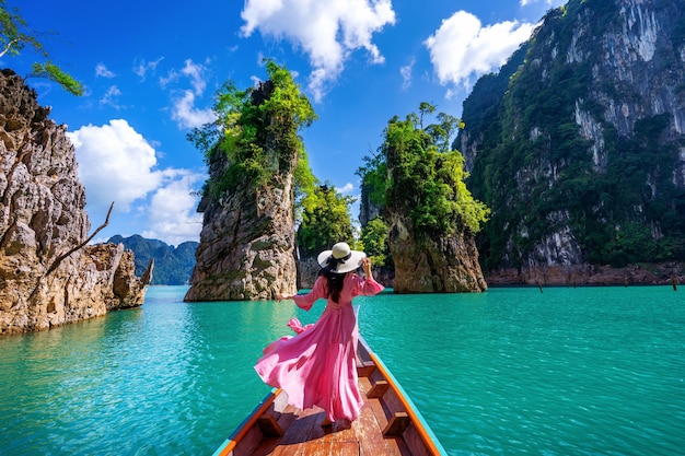 Free photo beautiful girl standing on the boat and looking to mountains in ratchaprapha dam at khao sok national park, surat thani province, thailand.