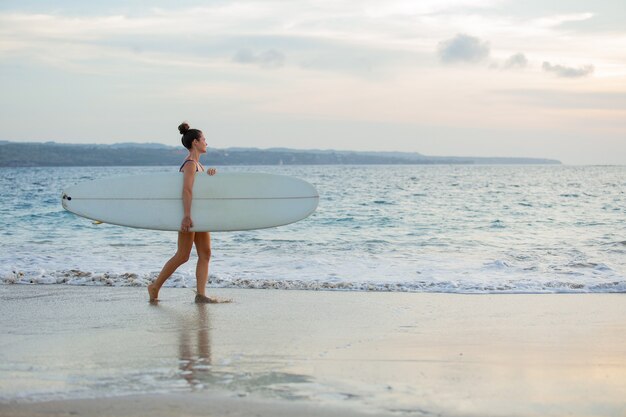 Beautiful girl stands on the beach with a surfboard.