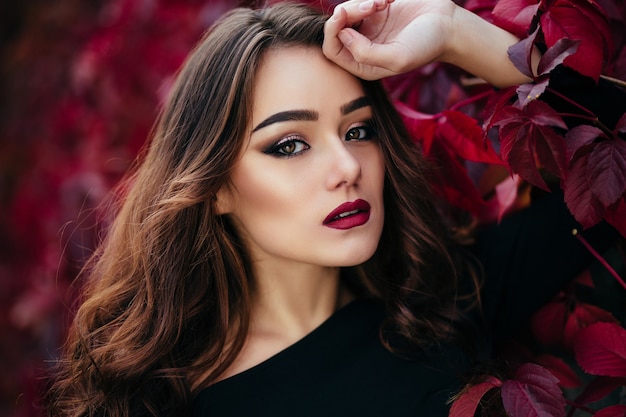 The beautiful girl stands near walll with leaves