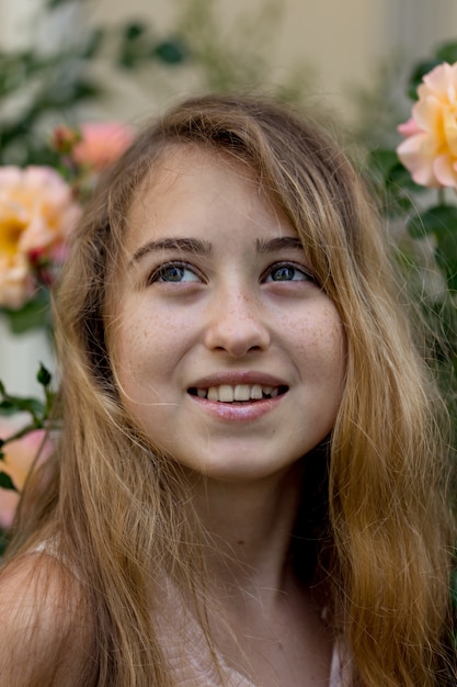 Beautiful girl staring and smiling near flowers outside during daytime .