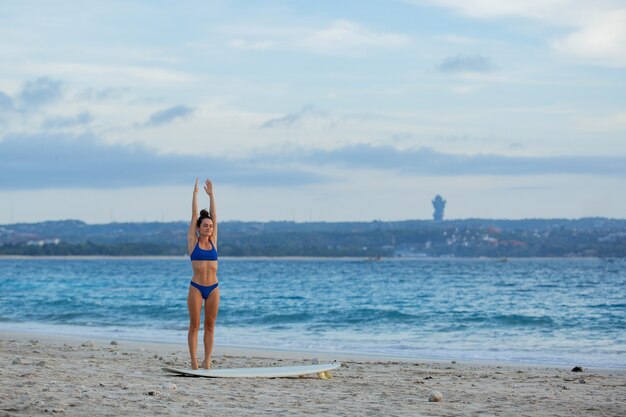 Beautiful girl stretching out on the beach with a surfboard.