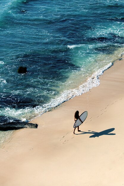 Beautiful girl walks with a surfboard on a wild beach. amazing view from the top.