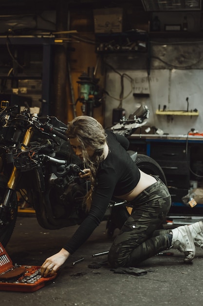 beautiful girl with long hair in the garage repairing a motorcycle