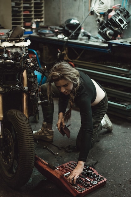 Free photo beautiful girl with long hair in the garage repairing a motorcycle