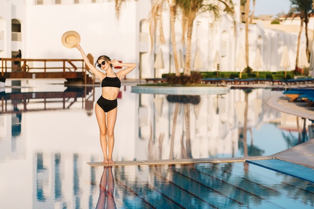 Free photo beautiful girl with slim body, model wearing black swimsuit posing in the middle of the pool in luxury hotel, resort. vacation, holiday, summertime.