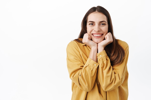 Free photo beautiful girlfriend with lovely smile, lean cute face on hands and watching something adorable, looking with admiration and interest, listening you, standing happy against white background