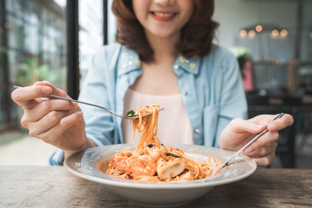 Beautiful happy Asian woman eating a plate of Italian seafood spaghetti at restaurant or cafe while 