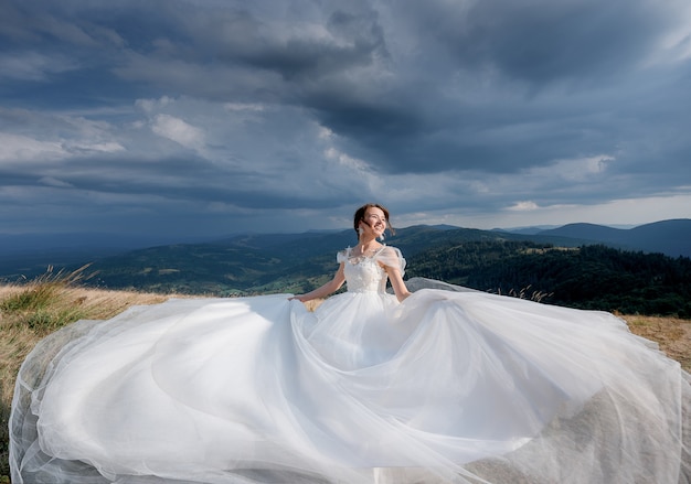 Beautiful happy bride dressed in luxury wedding dress on the sunny day in the mountains with the cloudy sky