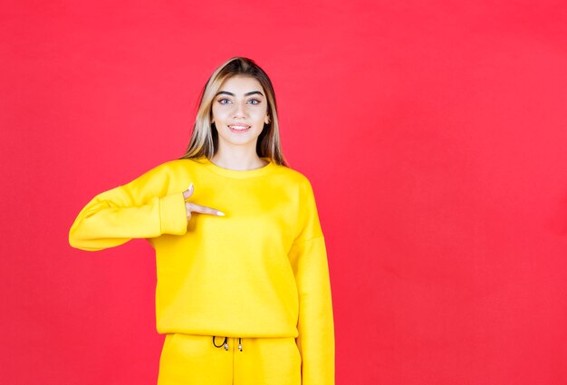 Free photo beautiful happy girl standing and pointing something on red wall