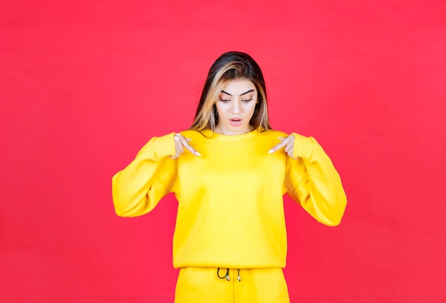 Free photo beautiful happy girl standing and pointing something on red wall