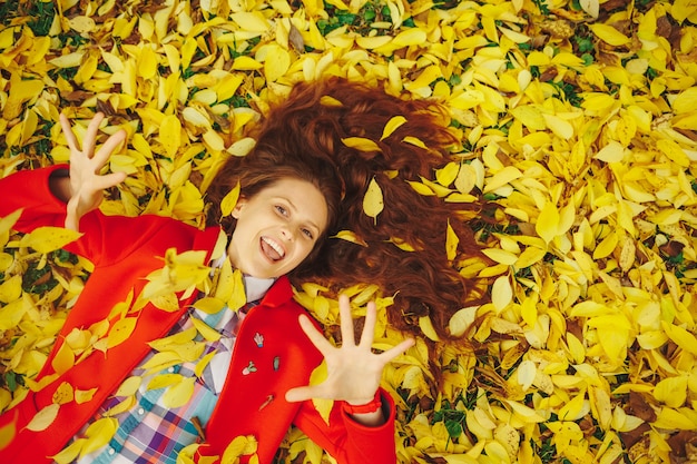 Beautiful happy woman laying in yellow autumn leaves.