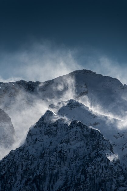 Beautiful high snowy and foggy mountains with snow being blown by wind