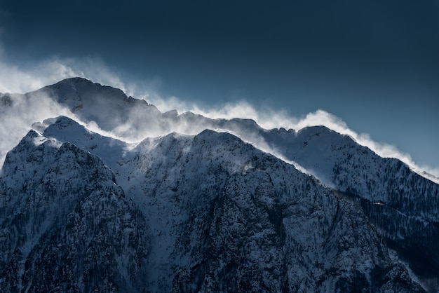 Beautiful high snowy and foggy mountains with snow being blown by wind