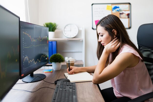 Free Photo beautiful hispanic woman taking notes while sitting at her work desk. professional woman working as a business analyst