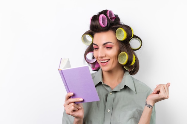 Beautiful housewife Young cheerful woman with curlers bright makeup with a book in her hands on a white background Thinking about a dinner recipe Looking for food ideas