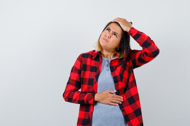 Beautiful lady in casual clothes holding hand on head, looking up and looking pensive , front view.