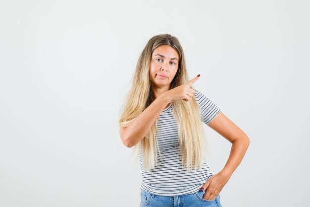 Beautiful lady pointing at left in t-shirt and looking displeased. front view.