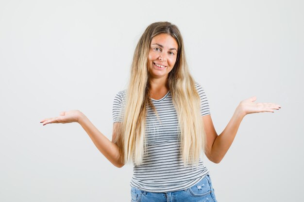 Beautiful lady raising hands for showing something in t-shirt and looking jolly , front view.