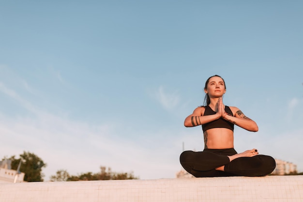 Beautiful lady sitting in lotus pose and dreamily looking aside. Young woman in black sporty top and leggings meditating while practicing yoga