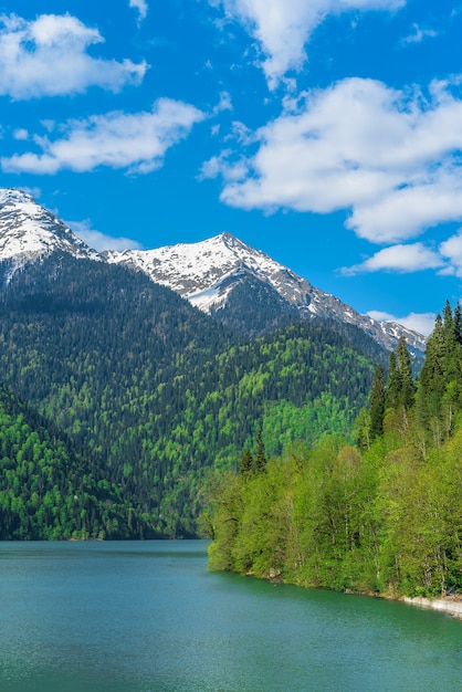 Beautiful Lake Ritsa in the Caucasus Mountains. Green mountain hills, blue sky with clouds. Spring landscape.