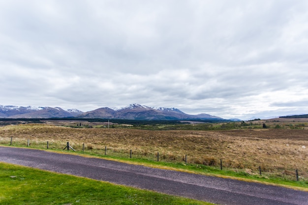 Free photo beautiful landscape with a road and high mountains covered in snow gleaming under the cloudy sky