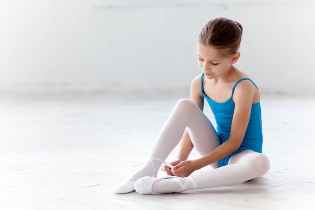 Beautiful little ballerina in blue dress for dancing puting on foot pointe shoes