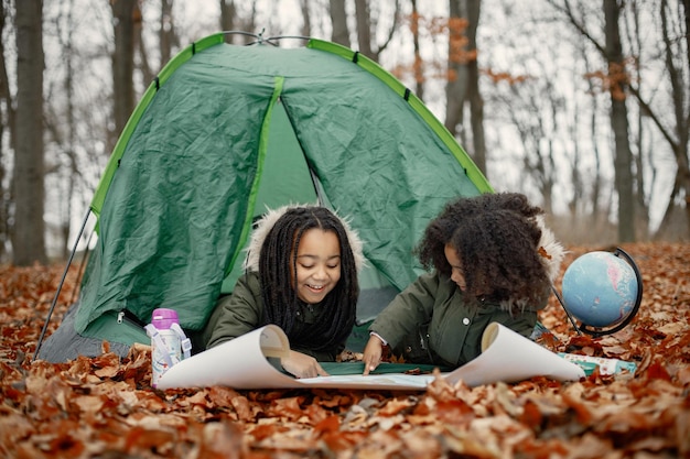 Free Photo beautiful little black girls in tent camping in the forest two little sisters lying in a tent in autumn forest and looking on a map black girls wearing khaki coats