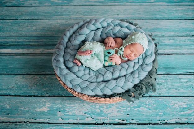 Free photo beautiful little girl sleeps with blue bear on blue blanket in the basket