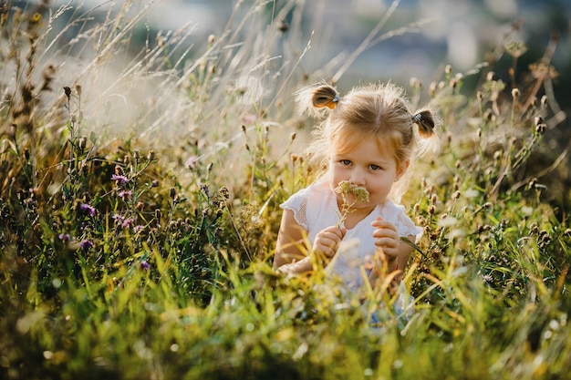 Beautiful little girl in white shirt and jeans sits  on the lawn with great landscape