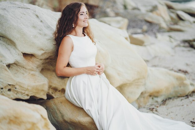 Beautiful long-haired bride in a magnificent white dress sitting near water