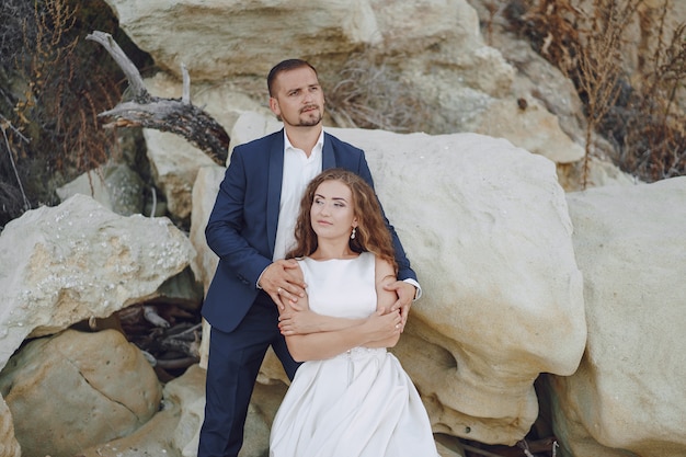 Free Photo beautiful long-haired bride in white dress with her husband on the beach near big stones