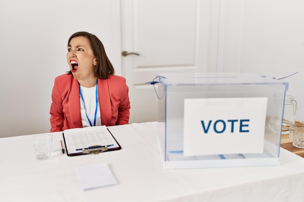 Free photo beautiful middle age hispanic woman at political election sitting by ballot angry and mad screaming frustrated and furious, shouting with anger. rage and aggressive concept.