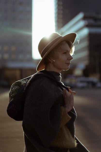 Beautiful middle-aged woman in a hat with a short haircut in the center of a big city. Close-up portrait, soft backlight.