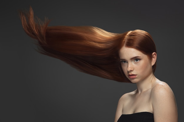 Beautiful model with long smooth, flying red hair isolated on dark