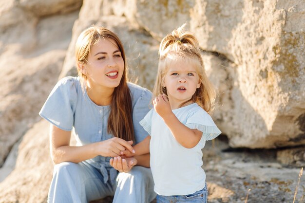 Beautiful mother and her cute long haired daughter are walking on meadow of stone